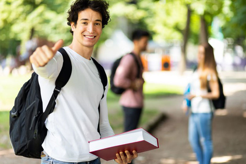 Alumno sosteniendo un libro levantando el pulgar